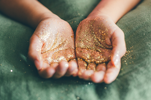 Girl hands holding golden glitter on a green linen fabric. Selective focus.