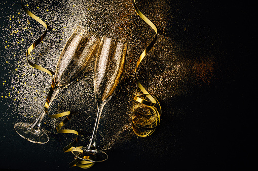 Two glasses of champagne toasting with golden confetti, glitter and serpentine on a dark background. Flat lay. Night of celebration concept