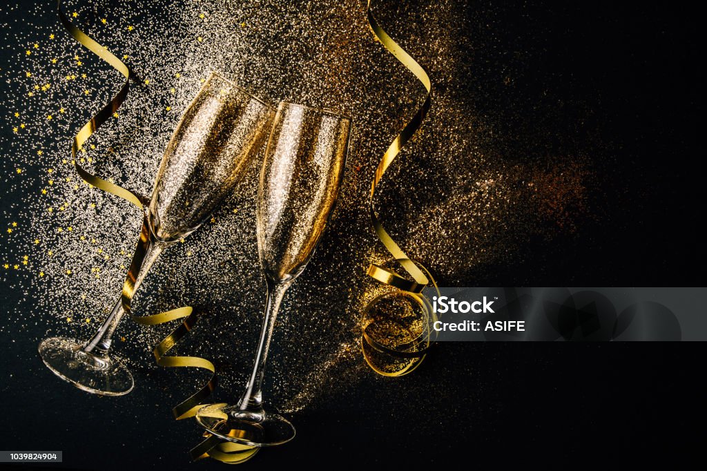 New year celebration party concept Two glasses of champagne toasting with golden confetti, glitter and serpentine on a dark background. Flat lay. Night of celebration concept New Year's Eve Stock Photo