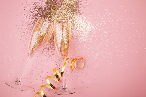Two glasses of champagne toasting with golden confetti, glitter and serpentine on a pink background. Flat lay. Night of celebration concept