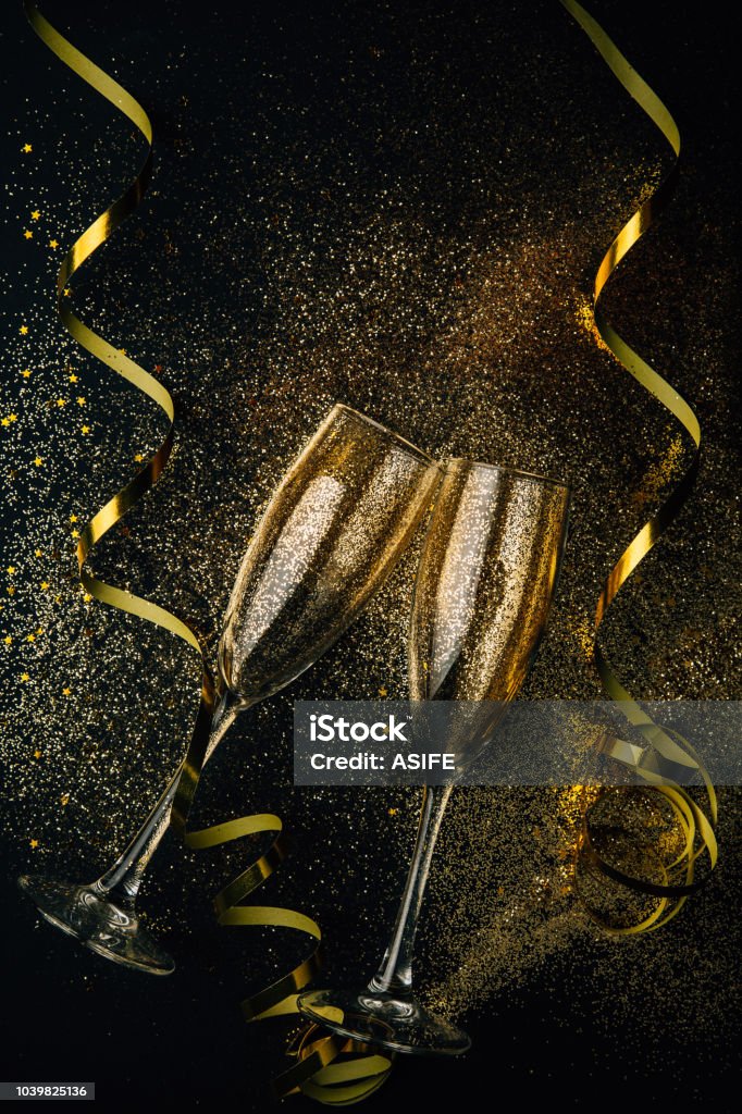 Toasting for the New Year Two glasses of champagne toasting with golden confetti, glitter and serpentine on a dark background. Flat lay. Night of celebration concept Champagne Stock Photo