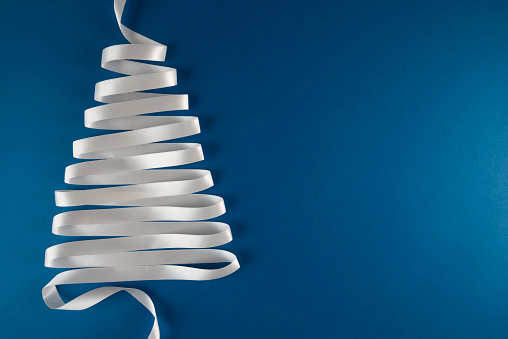 Christmas tree made of white ribbon on blue background.