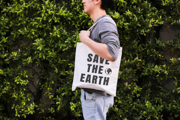 giovane hipster maschio che tiene e trasporta la borsa tote save the earth in sfondo ambiente naturale verde - ecologia e concetto di riciclo. - recycled bag foto e immagini stock