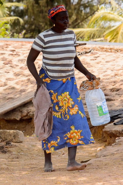 Unidentified Senegalese woman in striped shirt carries a plastic bottle on the coast of the Casamance river CASAMANCE RIVER, SENEGAL - APR 29: Unidentified Senegalese woman in striped shirt carries a plastic bottle on the coast of the Casamance river casamance river stock pictures, royalty-free photos & images