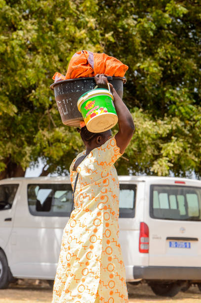 Unidentified Senegalese woman carries a basin and a bucket on her head on the coast of the Casamance river CASAMANCE RIVER, SENEGAL - APR 29: Unidentified Senegalese woman carries a basin and a bucket on her head on the coast of the Casamance river casamance river stock pictures, royalty-free photos & images
