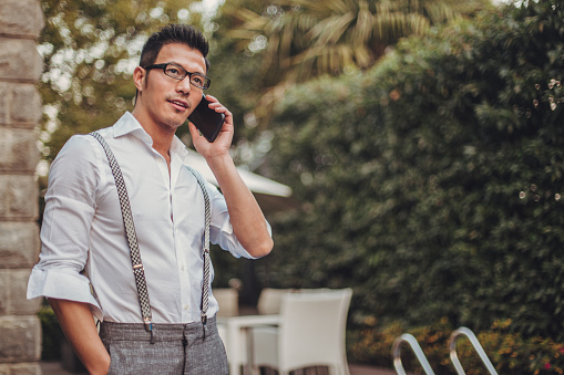 One man, standing in back yard by the swimming pool, using mobile phone.