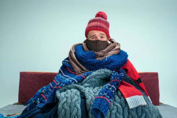 Bearded Man with Flue Sitting on Sofa at Home. Healthcare Concepts. Bearded sick man with flue sitting on sofa at home or studio covered with knitted warm clothes. Illness, influenza, pain concept. Relaxation at Home. Healthcare Concepts. cold and flu stock pictures, royalty-free photos & images