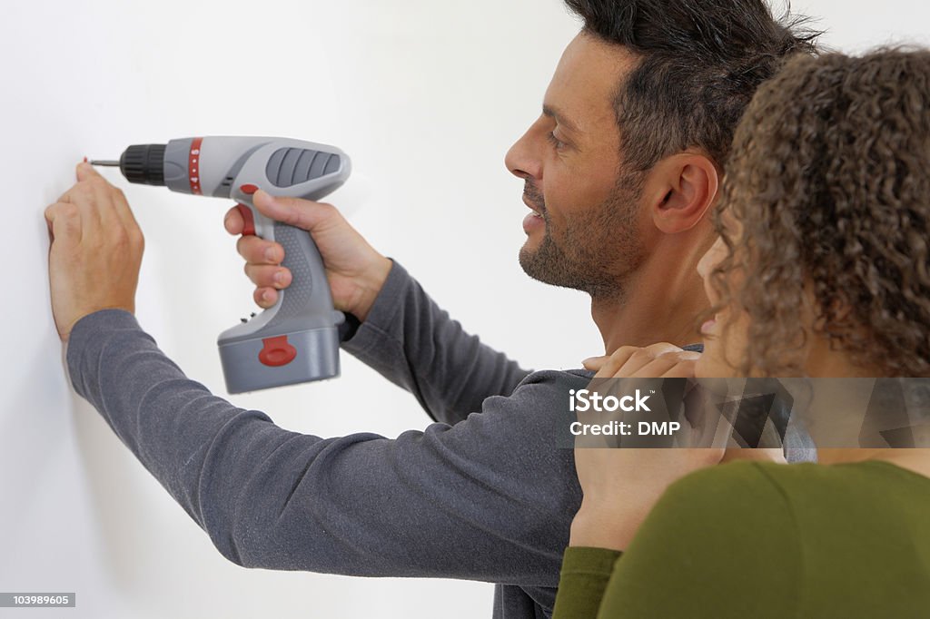 Junger Mann drilling Loch in Wand und Frau steht an - Lizenzfrei Attraktive Frau Stock-Foto