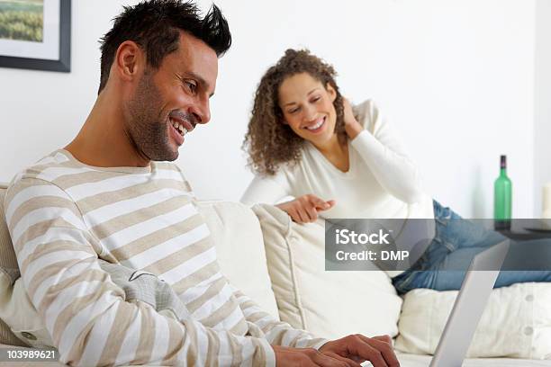 Junges Paar Sitzt Auf Sofa Mit Laptop Zu Hause Stockfoto und mehr Bilder von Arbeiten - Arbeiten, Attraktive Frau, Aussuchen
