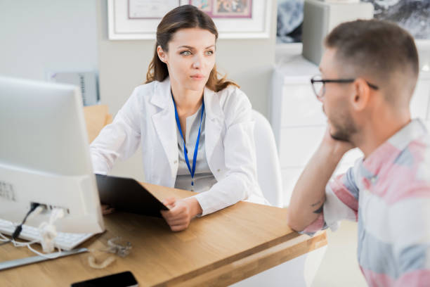 istock Content attractive female doctor in lab coat sitting at desk with computer and reading results of medical exam while working with patient 1039919812