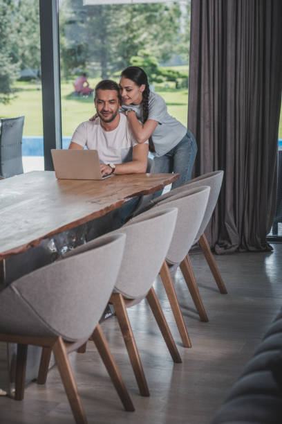 istock happy young woman embracing boyfriend while he using laptop at home 1039925214