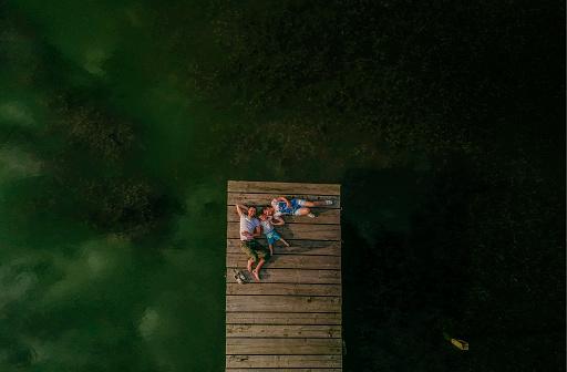 Photo of a young loving family enjoying their time by lying down on a dock of a lake