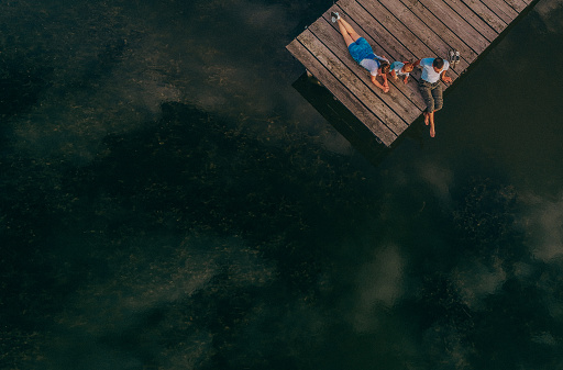 Photo of a young loving family enjoying their time by lying down on a dock of a lake