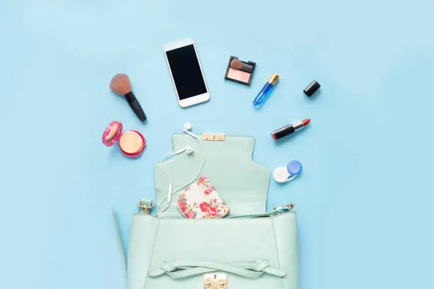 Photo of Topview of Fashionable female accessories watch glasses lipstick perfume and blue bag. Overhead of essentials for any girl, on blue background