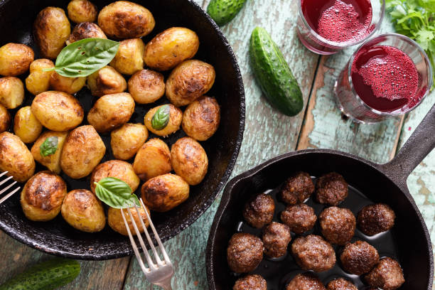 skandinaviska rätter. stekt potatis, köttbullar och lingon dryck serveras med grönsaker och örter på rustik blå tabell - potatis sweden bildbanksfoton och bilder