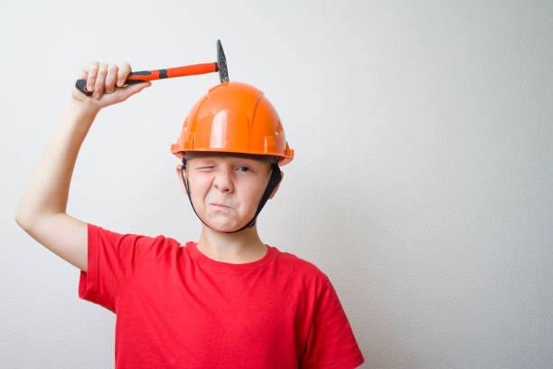 construction, protection, life safety fundamentals, brainstorming and creativity concept. Boy in helmet, hard hat. Young builder with hocked face knocks with hammer on head. copyspace