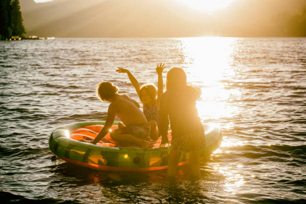 amigos y familiares jugando en una balsa inflable en un hermoso lago al atardecer - child inflatable raft lake family fotografías e imágenes de stock