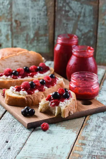 Tasty summer breakfast. Ciabatta toasts with homemade raspberry jam served with raw berries on shabby blue background copyspace