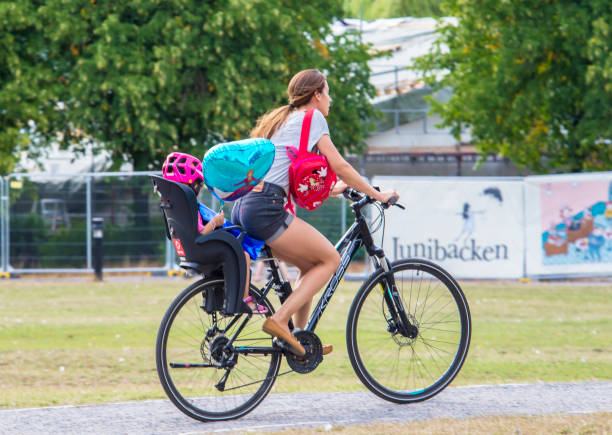 Stockholm, Sweden - 8/6/2018, 5:14:08 PM: Woman on bike in profile. Traffic in background in environment friendly Stockholm, Sweden. In sunshine after the rain.A woman rides a child on a bicycle