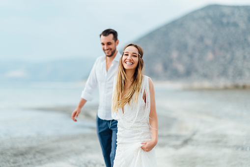 A young couple is walking happily by the water hand in hand.