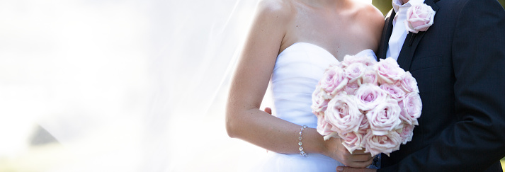 Newly married bride and groom posing with veil in a soft dreamy image in a garden