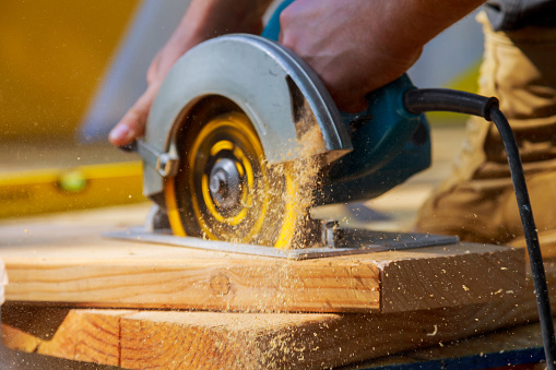 Carpenter using circular saw for cutting wooden boards with hand power tools.