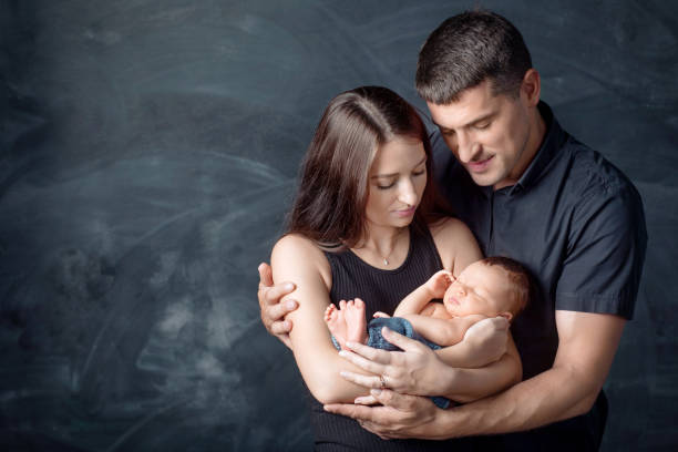Woman and man holding a newborn. Mom, dad and baby. Close-up. Portrait of  smiling family with newborn on the hands. Happy family on a background. stock photo