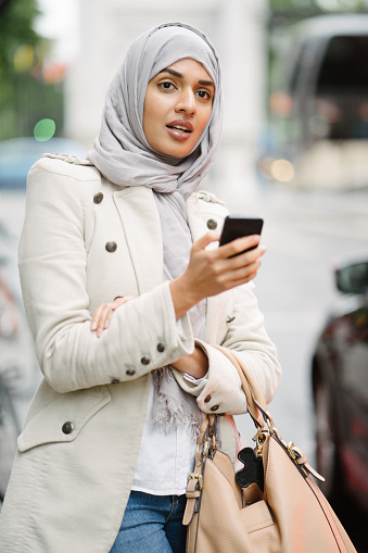 Beautiful woman checking her mobile phone while waiting for urban transportation.