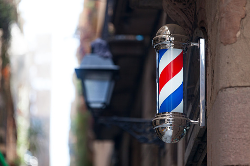 Barber's pole outside of a barber shop in a small street.