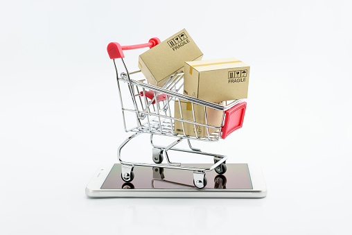 Online shopping and ecommerce via internet concept : Boxes in a shopping cart or metal trolley on a white mobile smartphone . Consumer always buy or shop goods and things from online retail stores .