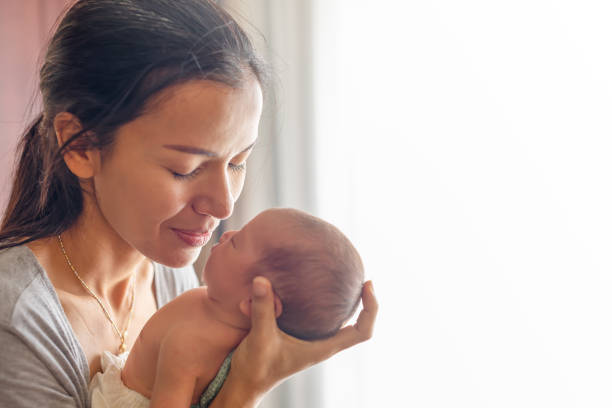 madre hermosa besos aquí poco lindo bebé en su palma. madre cuida a su niña en casa. muchacha recién nacida de una semana. - baby mother sleeping child fotografías e imágenes de stock