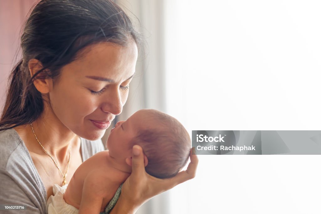 Linda mãe beijando aqui pouco bonito bebê na palma da mão. Mãe cuida de sua filhinha em casa. Menina recém-nascida de uma semana. - Foto de stock de Mãe royalty-free