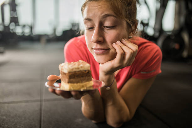 Young woman relaxing in a gym and thinking if she should eat a piece of cake or not.
