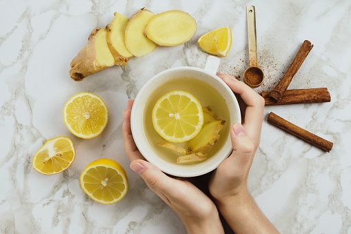 Flatlay of healthy drink with lemon, fresh ginger root, cinnamon sticks and agave syrup on marble background, natural cold or sore throat