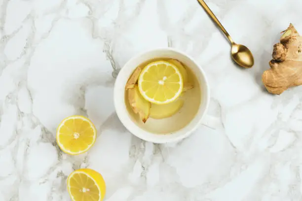 Photo of Flatlay of healthy drink with lemon and fresh ginger root on marble background, natural cold or sore throat