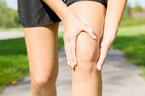 Photo of Young woman's hand touching her knee during running time on footpath. Joint pain. Sporty problem and solution. Close up. Front view.