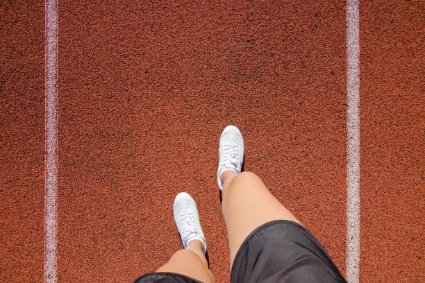 junge frau beine in weißen schuhen stehen im stadion verfolgen im sommertag. tägliche outdoor-aktiven lebensstil. genießen sport. trainingszeit. point of view erschossen. teil des körpers. - langstreckenlauf stock-fotos und bilder