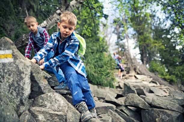 Mother and three kids hiking on very difficult trail. Family is walking through stones and rocks in forest.\nNikon D850