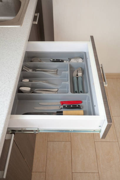 istock Profile side view vertical photo of part clean white cook worktop table and open new modern wooden kitchen drawer with different cutlery spoon, knife, fork and stuff 1040294032