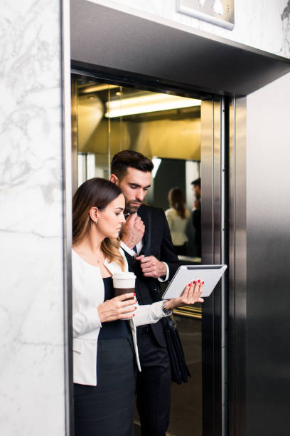 istock Business executives reading form device while walking out of elevator 1040294336