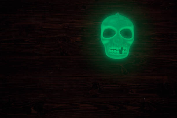 Halloween glowing phosphoric human skull over wooden table background. Neon light.