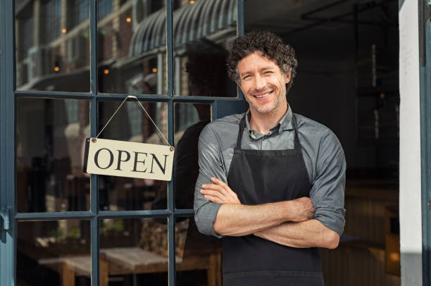 Owner standing outside restaurant Portrait of small business owner smiling and standing with crossed arms outside the cafe. Portrait of handsome smiling waiter standing in entrance of coffee shop. Successful mature man with arms crossed smiling at camera. cafeteria worker photos stock pictures, royalty-free photos & images