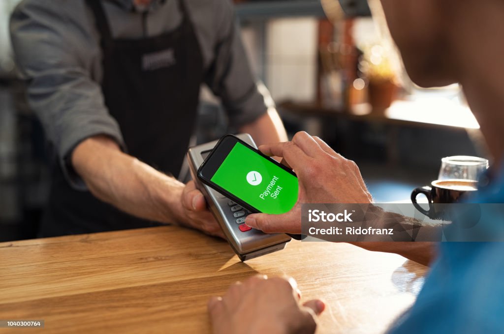 Payment with smartphone Customer paying bill through smartphone using NFC technology. Closeup of hand making payment through contactless machine. Woman hand holding mobile phone with green screen and paying the bill with contact less technology. Mobile Payment Stock Photo