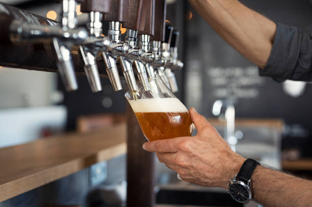Pouring beer in glass Hand of bartender pouring a large lager beer in tap. Closeup of hand serving beer in glass using tap. Close up of barman hand at beer tap pouring an amber draught beer at pub. man wearing a barrel stock pictures, royalty-free photos & images