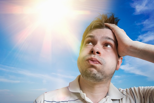 Young man is sweating. Hot weather concept. Sun in background.