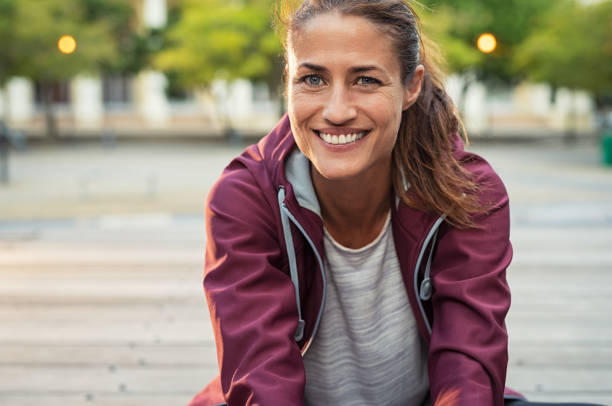 Smiling mature sporty woman Portrait of smiling woman sitting on floor of city street after running. Healthy mature runner resting after workout exercise and looking at camera. Active latin sporty woman enjoying outdoors in autumn. healthy lifestyle women outdoors athlete stock pictures, royalty-free photos & images