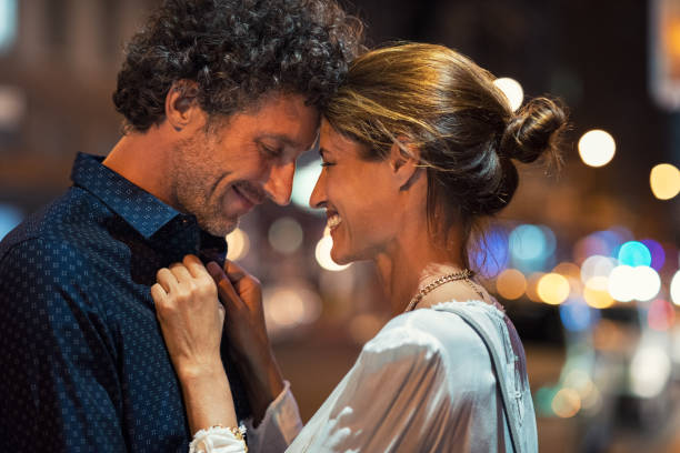 Mature couple in love at night Romantic man and woman on evening date. Happy husband and smiling wife embracing touching head to head on city street at night. Mature couple loving during a romantic night. flirting stock pictures, royalty-free photos & images