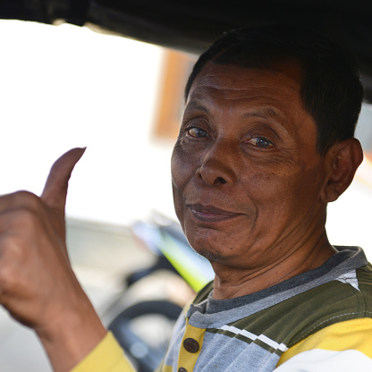 Local tuc tuc driver inside his vehicle on a sunny day in Jakarta, Indonesia