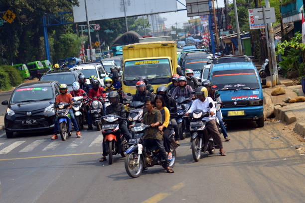 Locals riding scooters and motorbikes in heavy traffic on a sunny day in Jakarta, Indonesia
