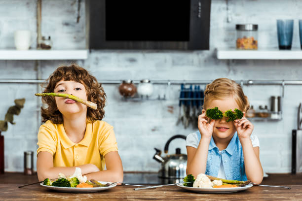 adorable children playing with vegetables while sitting together at table adorable children playing with vegetables while sitting together at table eating asparagus stock pictures, royalty-free photos & images